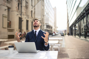 Man sitting at outdoor table with laptop and coffee